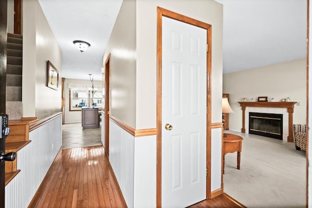 hall with a wainscoted wall, stairway, wood-type flooring, and a chandelier