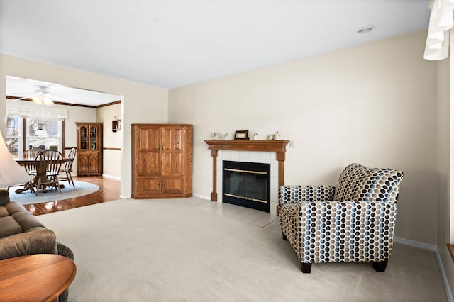 living area featuring ceiling fan, carpet, baseboards, ornamental molding, and a tiled fireplace