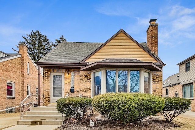 view of front of property with brick siding, a chimney, and roof with shingles