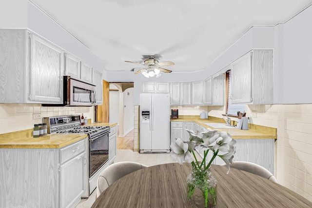 kitchen featuring a sink, stainless steel microwave, white refrigerator with ice dispenser, range with gas cooktop, and light countertops