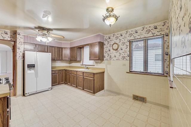 kitchen featuring visible vents, a sink, wallpapered walls, white refrigerator with ice dispenser, and light countertops