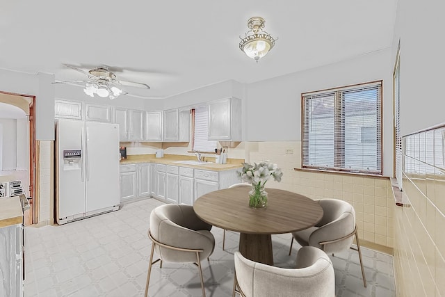 dining room featuring a ceiling fan, tile walls, light floors, and wainscoting