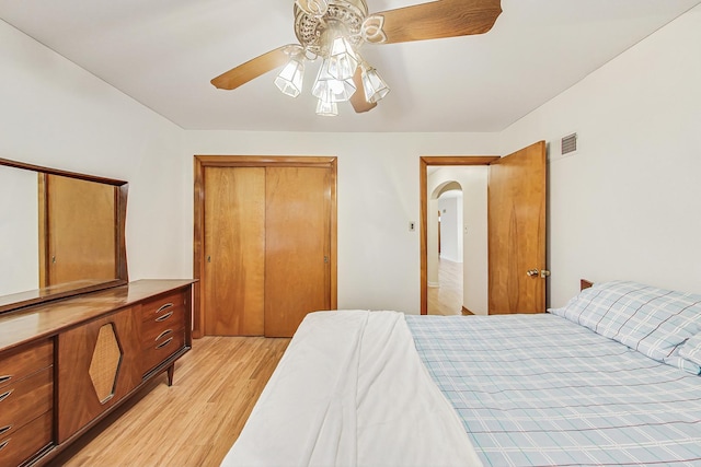 bedroom with a ceiling fan, visible vents, light wood-style flooring, arched walkways, and a closet