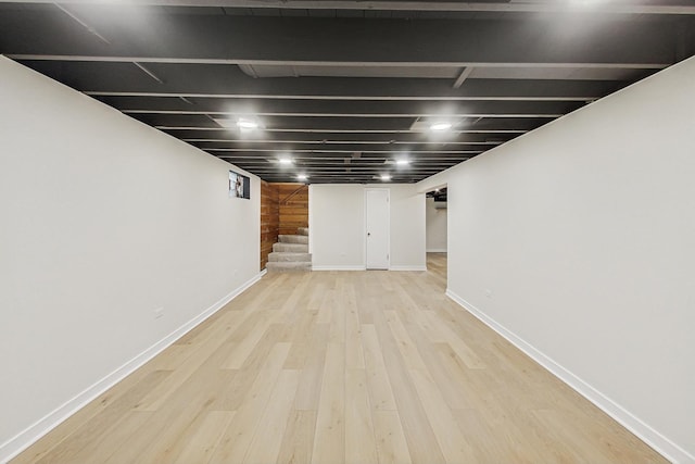 finished basement featuring stairway, baseboards, and light wood-style flooring