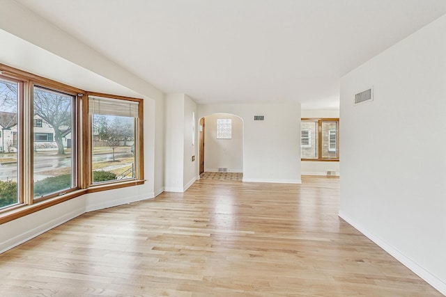 unfurnished room with visible vents, arched walkways, light wood-style floors, and baseboards