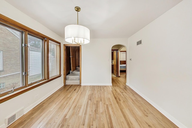 unfurnished room with light wood-type flooring, visible vents, baseboards, and arched walkways