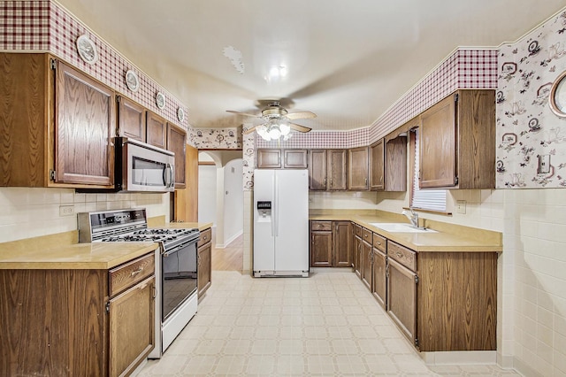 kitchen with a sink, stainless steel microwave, range with gas stovetop, white refrigerator with ice dispenser, and arched walkways