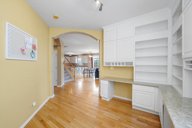 hallway with arched walkways, baseboards, stairs, and light wood-style floors