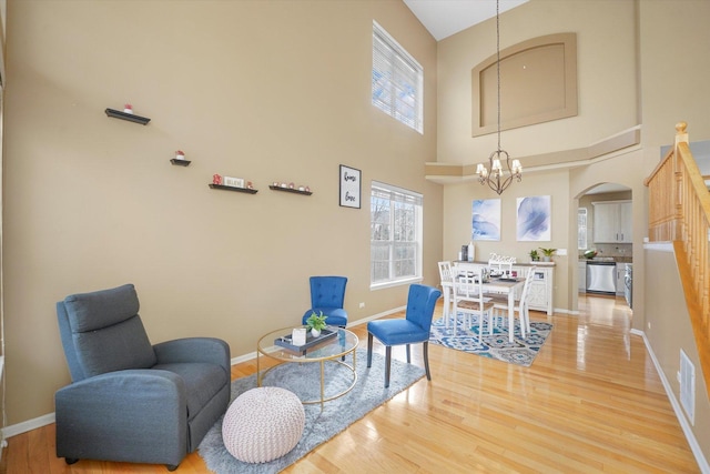 sitting room with baseboards, arched walkways, a high ceiling, light wood-type flooring, and a notable chandelier