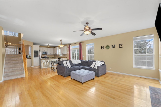 living area with baseboards, arched walkways, a ceiling fan, stairs, and light wood-type flooring