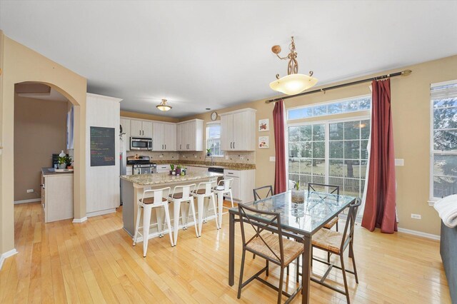 dining area featuring light wood-type flooring, baseboards, and arched walkways