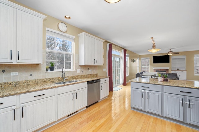 kitchen featuring a sink, light wood-style floors, open floor plan, a brick fireplace, and dishwasher