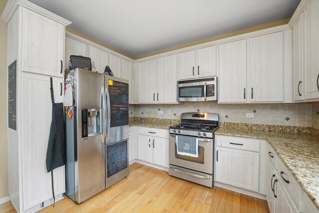 kitchen with light stone counters, tasteful backsplash, appliances with stainless steel finishes, light wood-style floors, and white cabinetry