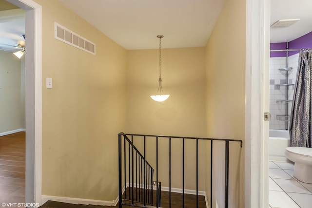 hall featuring tile patterned floors, visible vents, baseboards, and an upstairs landing