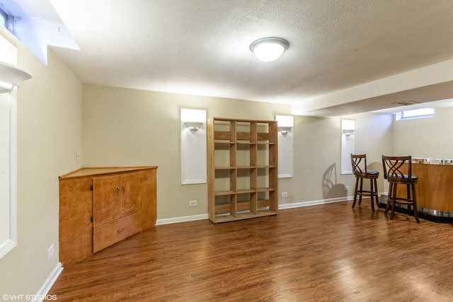 below grade area with baseboards, a textured ceiling, wood finished floors, and a bar