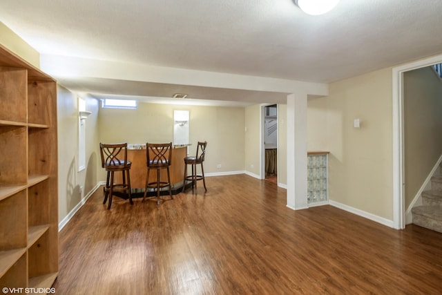 sitting room with a bar, stairs, baseboards, and wood finished floors