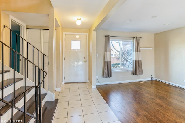 foyer with light wood finished floors, stairway, visible vents, and baseboards