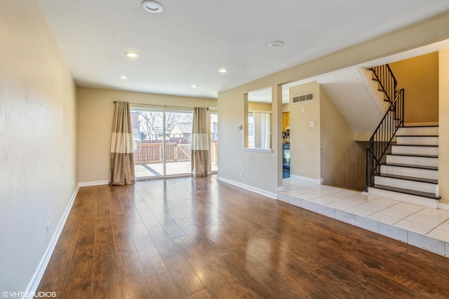 unfurnished living room featuring visible vents, baseboards, wood finished floors, and stairway