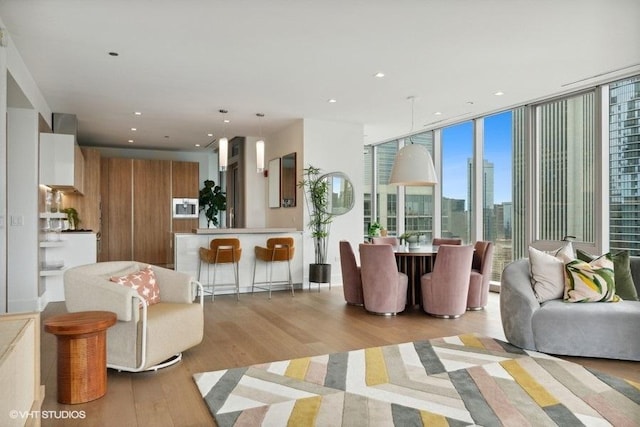 living room with light wood-type flooring, a view of city, floor to ceiling windows, and recessed lighting