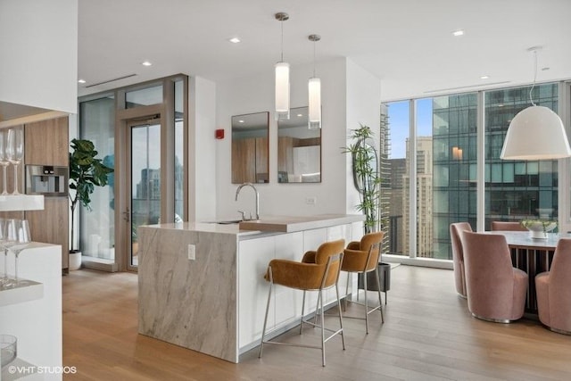 kitchen with pendant lighting, light wood finished floors, a sink, and floor to ceiling windows