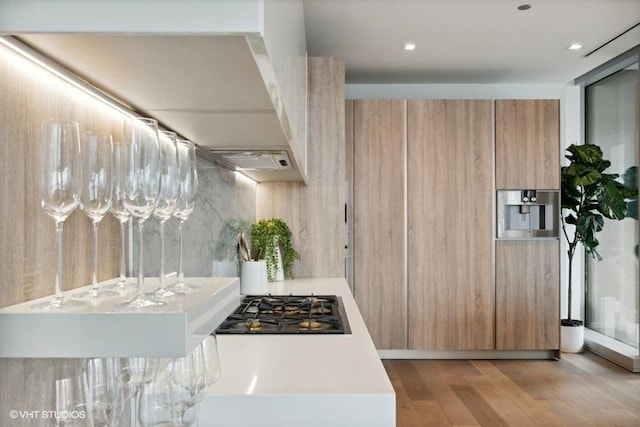 kitchen with wood finished floors, light countertops, stainless steel gas stovetop, light brown cabinetry, and modern cabinets