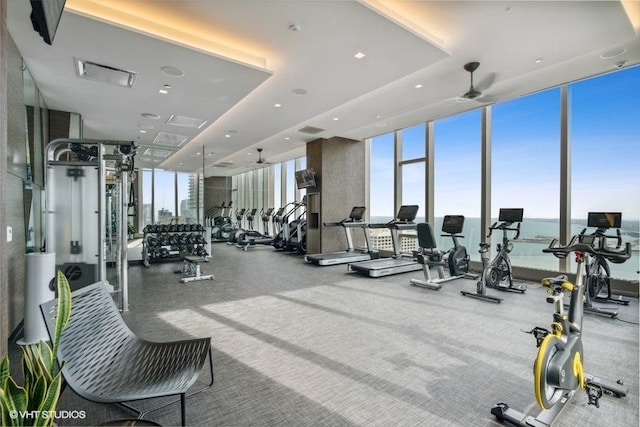 exercise room with a wall of windows, a raised ceiling, visible vents, and a ceiling fan