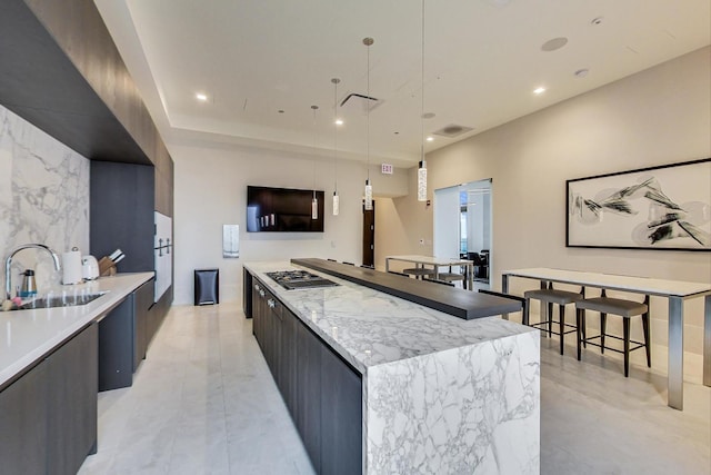 kitchen featuring a spacious island, modern cabinets, hanging light fixtures, stainless steel gas cooktop, and a sink