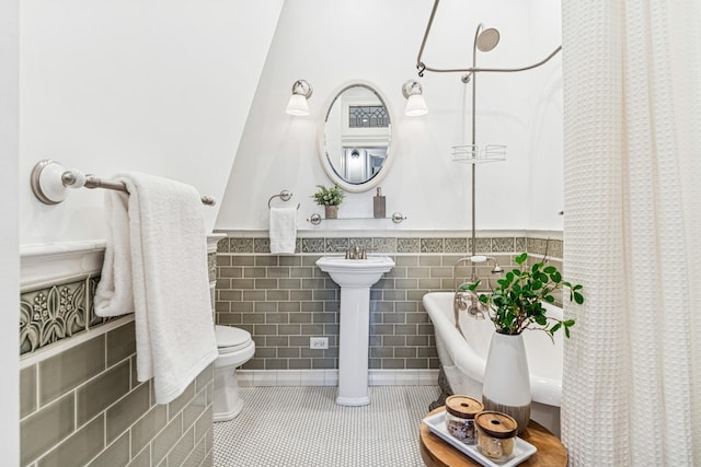 bathroom featuring tile patterned flooring, a freestanding bath, toilet, tile walls, and wainscoting