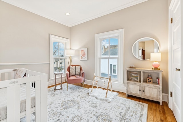 bedroom with a crib, baseboards, wood finished floors, and crown molding