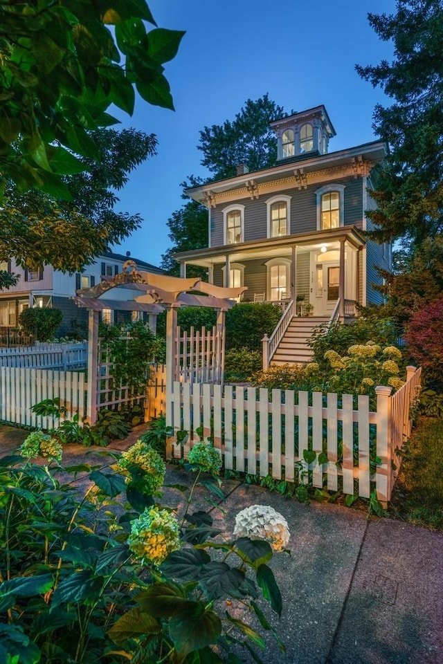 view of front facade with stairway, covered porch, and a fenced front yard