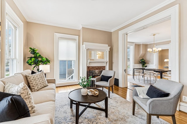 living room with a fireplace, light wood finished floors, ornamental molding, and an inviting chandelier