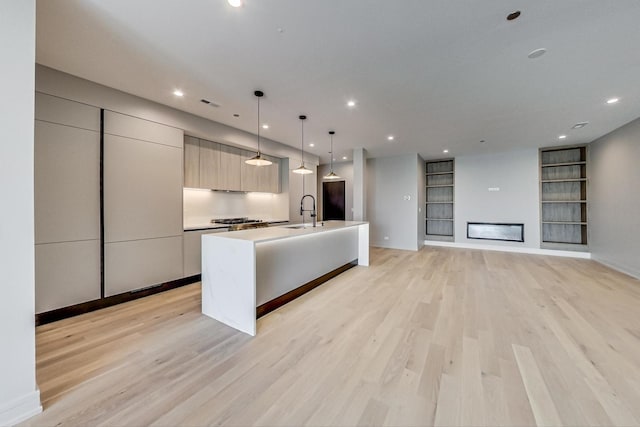 kitchen featuring visible vents, an island with sink, modern cabinets, built in shelves, and light wood finished floors