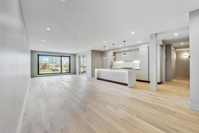 unfurnished living room with baseboards, a sink, and light wood finished floors