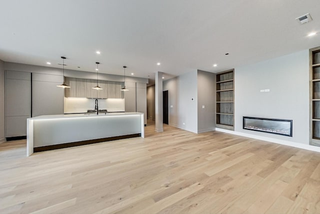 unfurnished living room featuring recessed lighting, baseboards, built in shelves, and light wood-type flooring