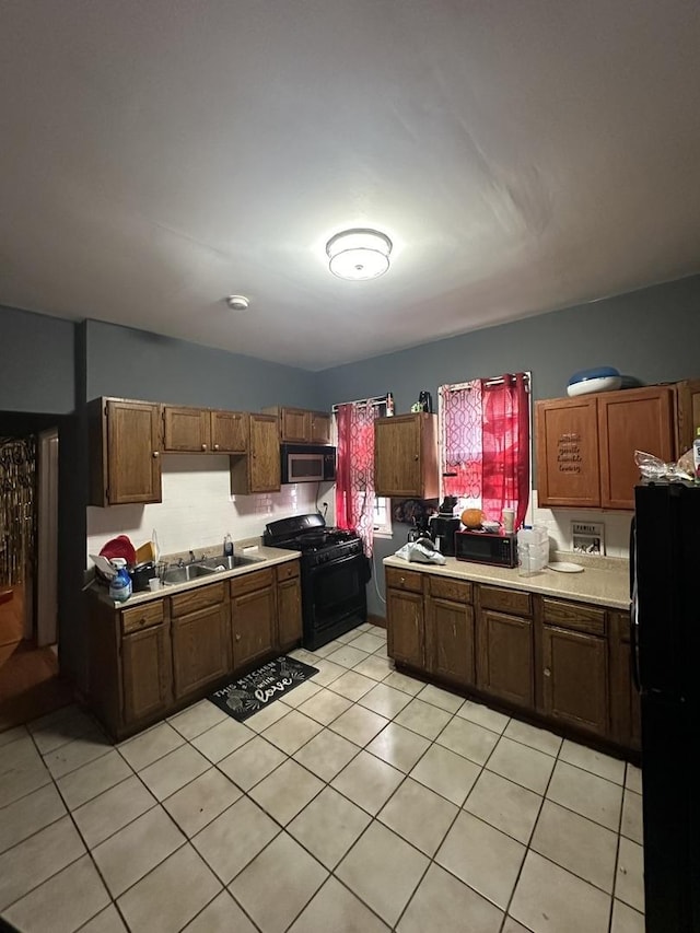 kitchen featuring a sink, black appliances, light tile patterned floors, and light countertops