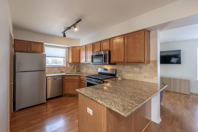 kitchen with light stone counters, appliances with stainless steel finishes, a peninsula, and brown cabinetry