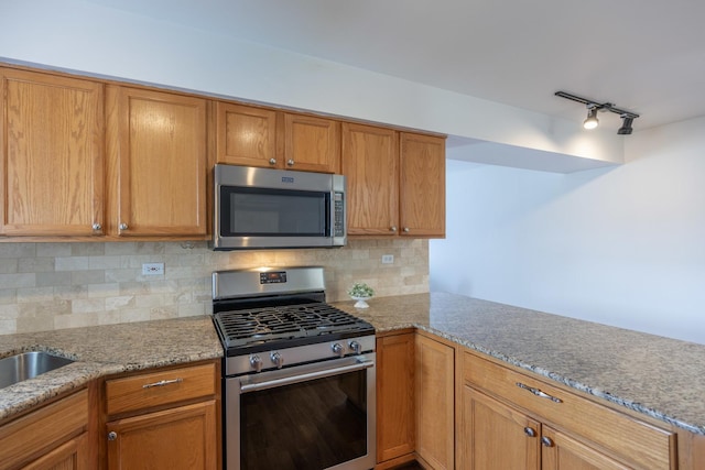 kitchen with light stone counters, brown cabinets, a peninsula, appliances with stainless steel finishes, and tasteful backsplash