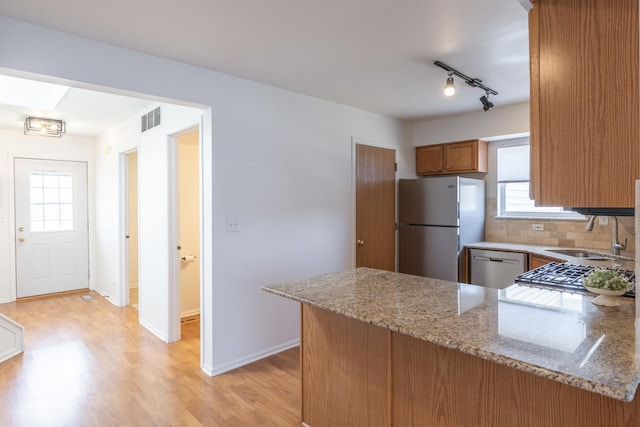 kitchen with light stone countertops, a peninsula, a sink, appliances with stainless steel finishes, and brown cabinets