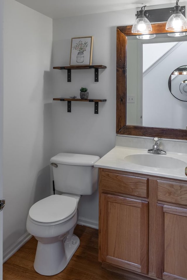 bathroom featuring baseboards, toilet, wood finished floors, and vanity