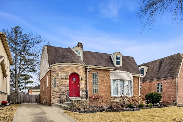 view of front of house featuring stone siding, brick siding, a chimney, and fence