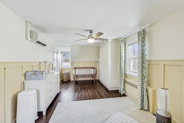 bedroom featuring a ceiling fan, dark wood-type flooring, wainscoting, and a wall mounted AC