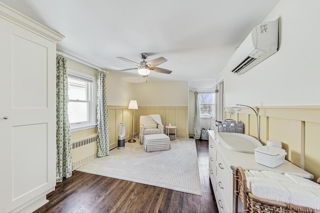 sitting room with radiator, ceiling fan, an AC wall unit, wainscoting, and wood finished floors