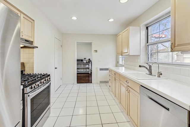 kitchen featuring radiator, light tile patterned flooring, a sink, under cabinet range hood, and appliances with stainless steel finishes