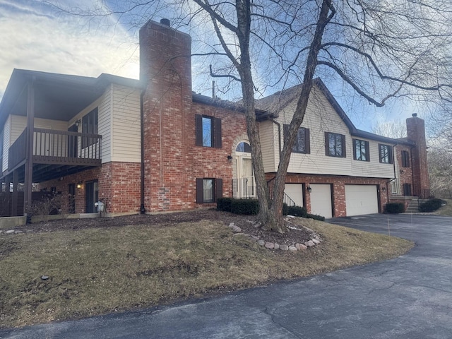 view of home's exterior with an attached garage, a chimney, aphalt driveway, and brick siding