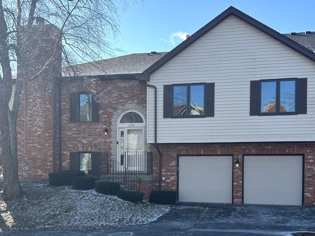 raised ranch featuring a garage, driveway, and brick siding