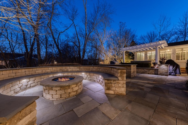 patio at night with area for grilling, a fire pit, and a pergola