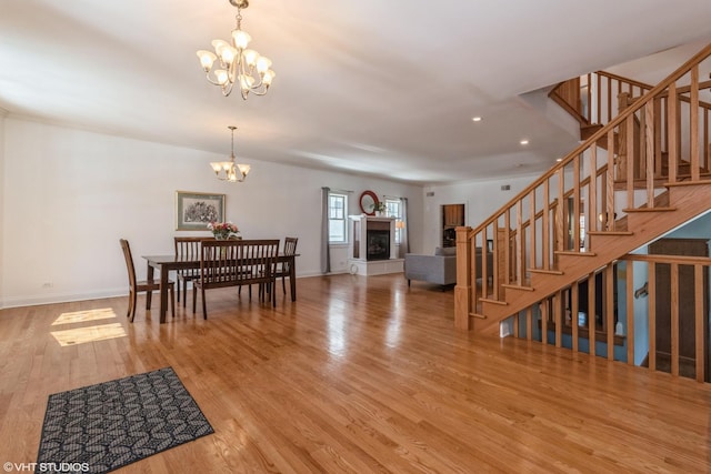 dining area featuring baseboards, a fireplace with raised hearth, stairway, wood finished floors, and an inviting chandelier