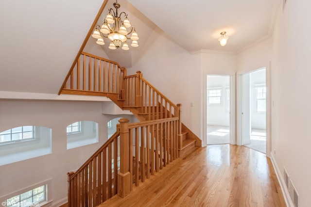 staircase with a chandelier, wood finished floors, visible vents, baseboards, and crown molding