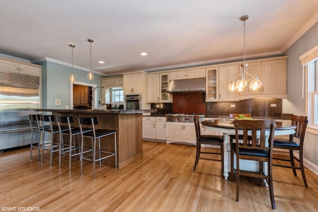 kitchen with under cabinet range hood, appliances with stainless steel finishes, tasteful backsplash, dark countertops, and a kitchen bar