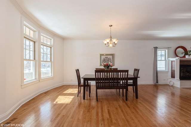 dining room with light wood-type flooring, baseboards, ornamental molding, and a glass covered fireplace